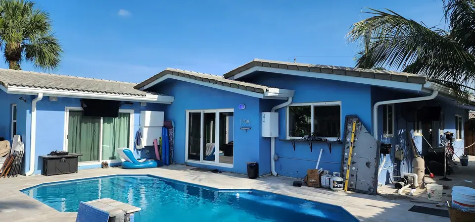 A blue stucco home with white gutters behind a pool