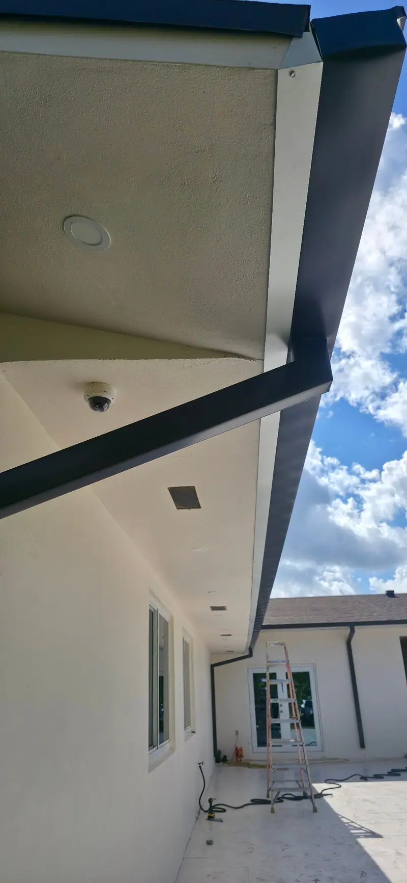 A small dome security camera mounted under a white soffit next to a dark gutter
