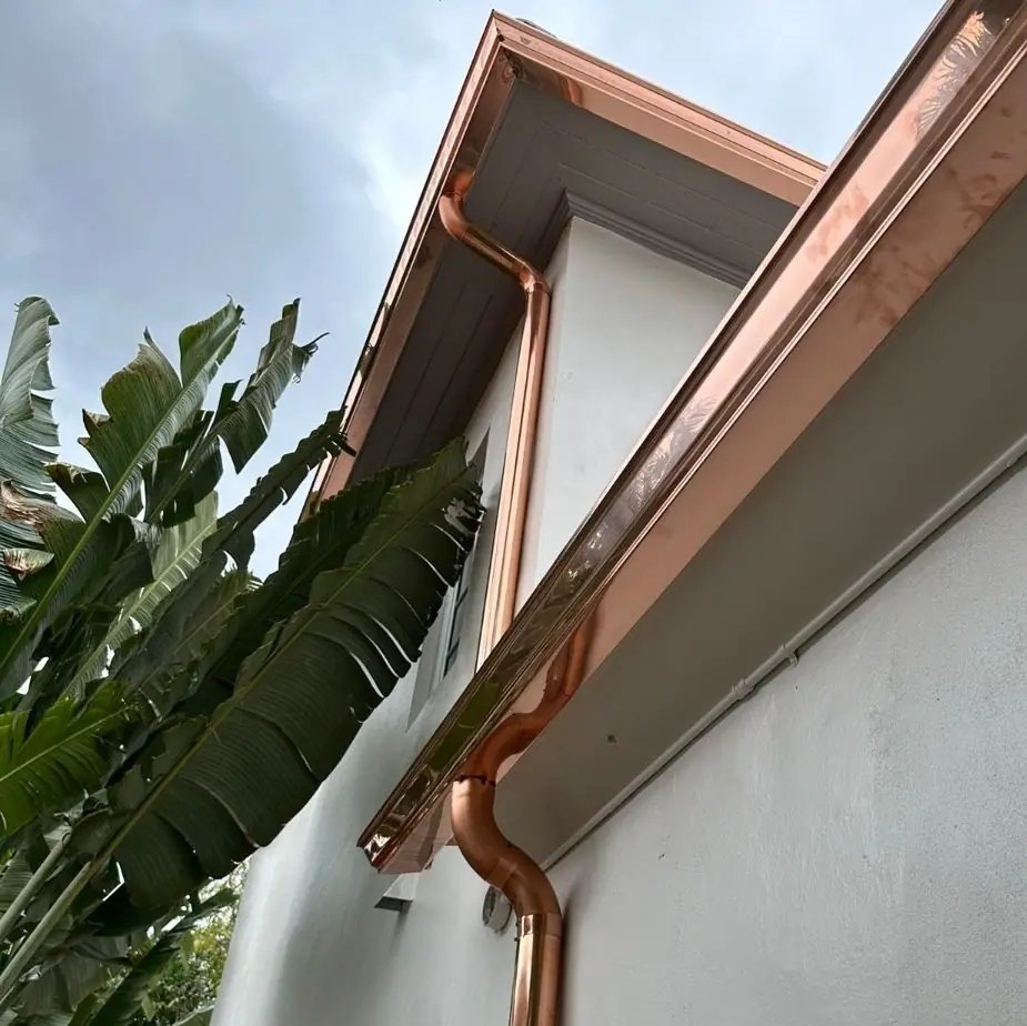 A copper seamless gutter and downspout on a white stucco wall