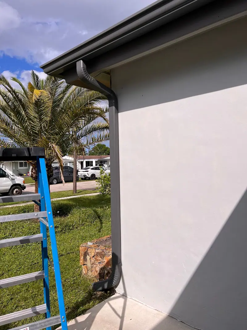A new dark gutter and downspout on grey stucco, with the ladder still up