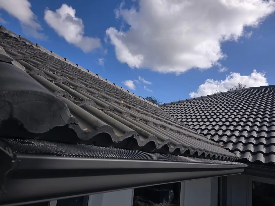 A gutter along a black concrete tile roof under a blue sky