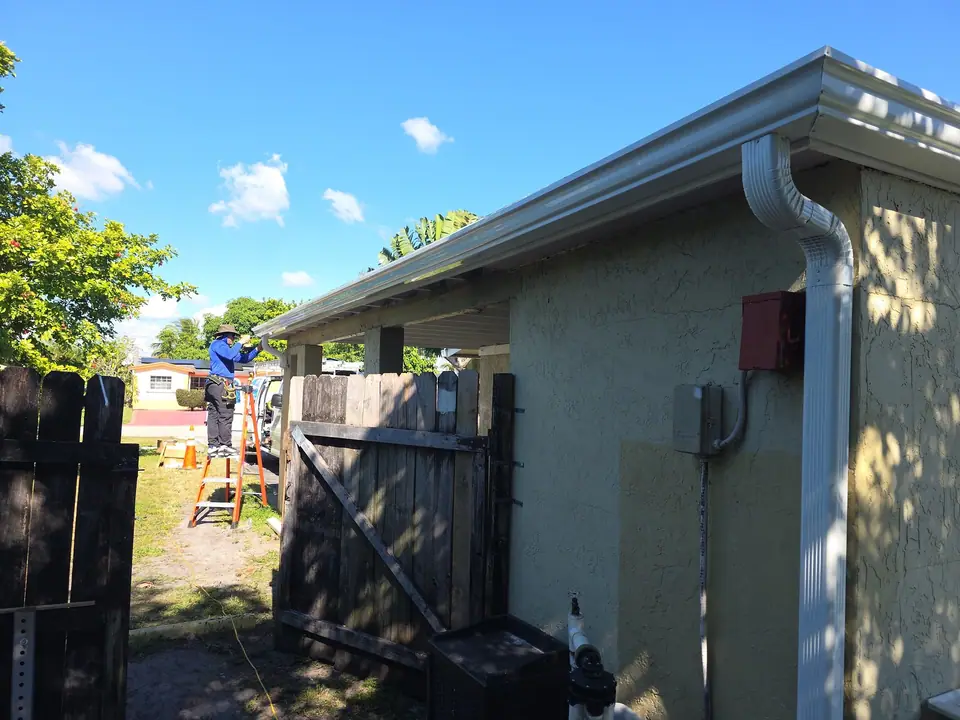A white gutter and downspout on a stucco home, with the crew at work by the gate