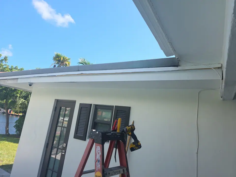 Working on a white eave with a ladder and a drill before the gutter goes up