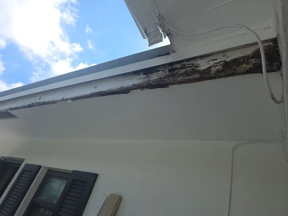 Rotted fascia board along a white eave, before repair