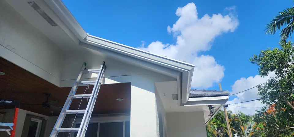 A ladder at the eave of a white home with new white gutters
