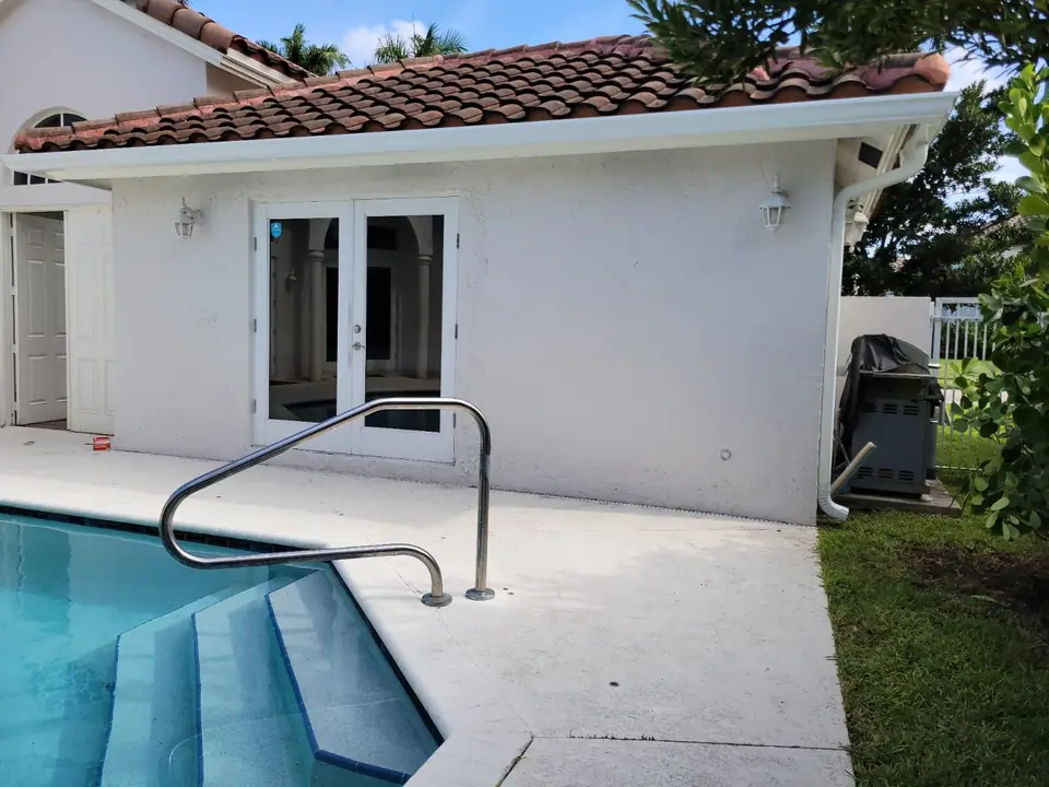 A white tile-roof home with a new gutter over the pool steps