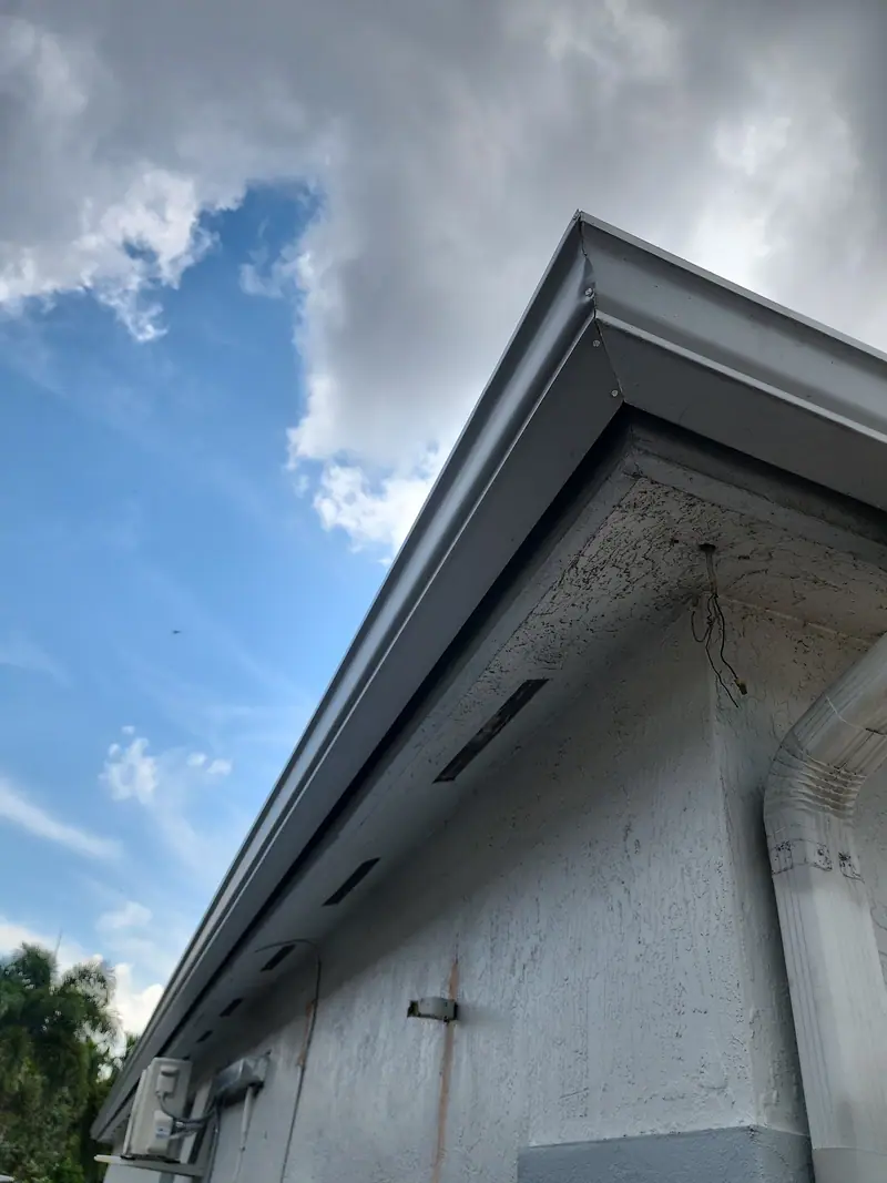 A white seamless gutter run along a stucco home, seen from below against the sky