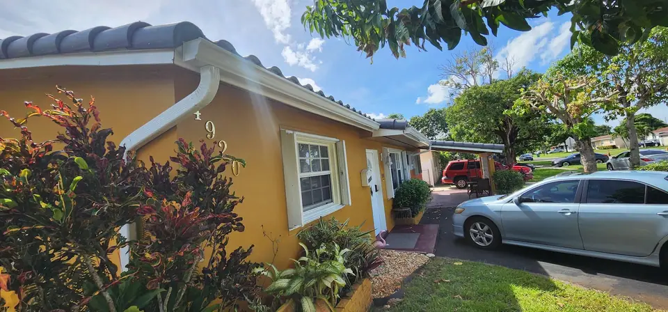 A white gutter on a yellow stucco ranch home with tropical plants